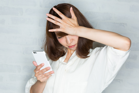 スマホを見てショックを受ける女性